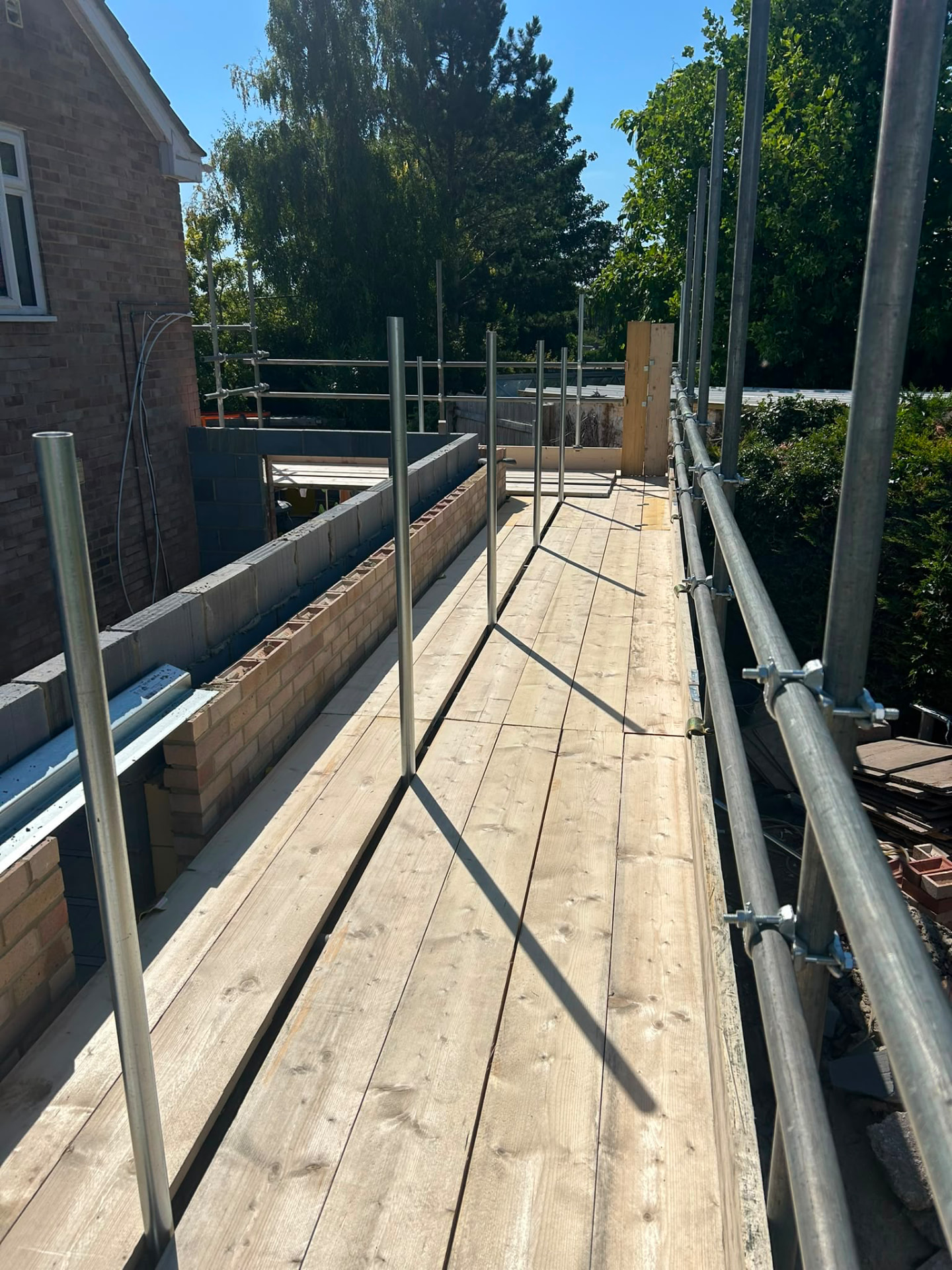 Fully boarded scaffold working platform with double guardrails running alongside new blockwork on a house extension